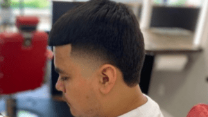 A person with a fade haircut and short bangs sits in a room with a blurred background, showcasing the precision of great barbers near me.