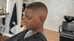 A young boy sits in the barber chair with a fresh haircut, showcasing a fade and short top, in a cozy barber shop near me.