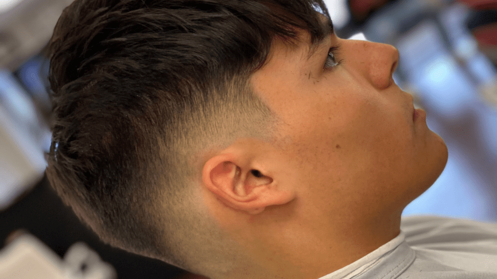 A person with dark hair sits in a salon chair, showcasing a close-up of a fresh fade haircut with layered top by one of the great barbers near me.